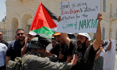 Seorang demonstran Palestina memegang plakat selama protes yang menandai ulang tahun ke-71 Hari 'Nakba', atau 'bencana', dan terhadap Eurovision Song Contest yang diselenggarakan oleh Israel, di Betlehem di Tepi Barat yang diduduki Israel 15 Mei 2019. (Foto: Reuters/Mussa Qawasma)