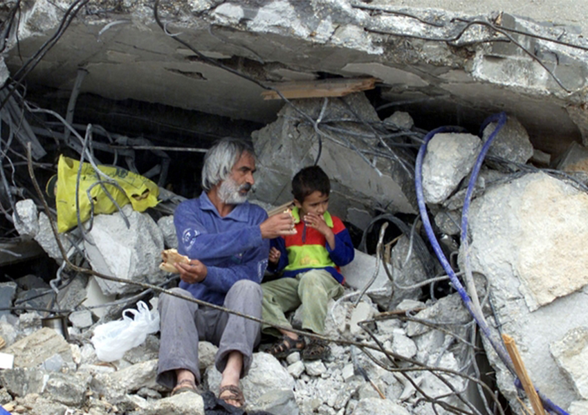Seorang pria Palestina memberikan roti kepada anak laki-laki di sisa-sisa rumah mereka yang hancur di kamp pengungsian Jenin 20 April 2002 (Foto: Reuters)